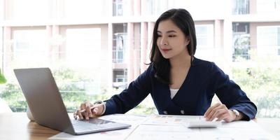 Happy young asian businesswoman sitting on her workplace in the office. Young woman working at laptop in the office. photo