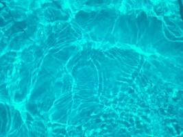 Defocus blurred transparent blue colored clear calm water surface texture with splashes and bubbles. Trendy abstract nature background. Water waves in sunlight. Blue water background. photo