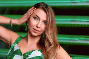 Portrait of stylish brown hair woman in green dress, green earrings, with makeup on green background in photostudio. Femininity, womanhood, travel, fashion concept photo