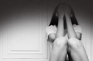 Asian woman with hands on her face, crying while sitting on the floor, feeling sad tired and suffer from major depressive disorder. Mental health or psychological concept. Black and white tone photo