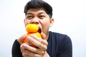 atractivo hombre asiático comiendo naranjas. aislado sobre fondo blanco foto