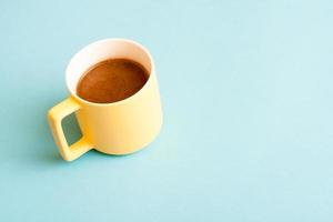 Simple concept yelow cup of fresh hot coffee on blue background. photo