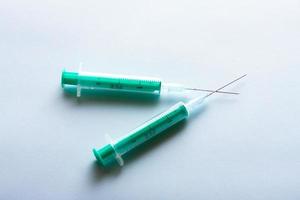 A pair of green medical syringes on bright blue background. photo