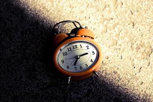 Vintage style orange alarm clock under the bright light and dark shadow. photo