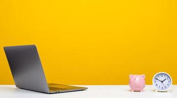 Desk with laptop with clock and piggy bank, designer workspace with copy space. photo