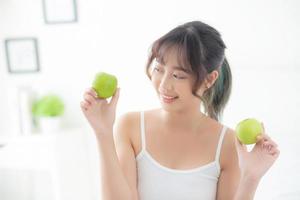 hermoso retrato joven mujer asiática sosteniendo y comiendo fruta de manzana verde en el dormitorio en casa, estilo de vida de nutrición niña saludable y cuidado concepto de pérdida de peso, salud y bienestar. foto