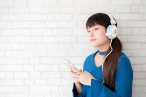 hermoso retrato mujer joven asiática de pie feliz disfrutar y divertirse escuchar música con auriculares sobre fondo de hormigón de cemento, estilo de vida de chica relajar radio de sonido con auriculares, concepto de tecnología. foto