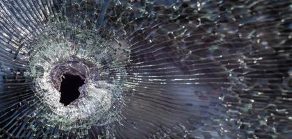 Bullet hole in glass with cracks, real bullet hole close-up. The bullet made a cracked hole in the windshield of a car or a window glass shattered as a result of an accident. Banner with copy space. photo