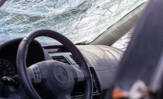 primer plano del volante de un coche después de un accidente. las bolsas de aire del conductor no se desplegaron. enfoque suave. parabrisas roto con volante. interior del vehiculo salpicadero y volante negros. foto