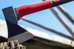 A new modern ax with a red handle sticks out of a wooden stump against a green meadow on a summer sunny day. The ax stuck into the stump. Ax blade in a log. photo