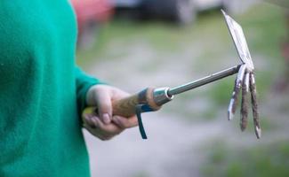 Caucasian woman gardener in the garden shows a rake. The concept of gardening and sustainable summer. Woman's hand with a garden tool. Chopper rake for gardening in female hands. Place for text. photo