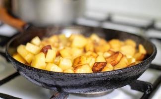 Roasting fresh potatoes in a cast iron skillet with sunflower oil. A view of a stovetop with a frying pan filled with golden fried potatoes in a real kitchen. Food cooked in a homemade frying pan. photo