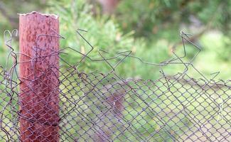 Mesh old ragged cage in the garden and a rusty pole with green grass as a background. Metal fence with wire mesh. Metal fence made of steel iron mesh. Abstract background. copy space. photo