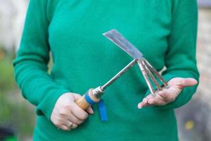 Caucasian woman gardener in the garden shows a rake. The concept of gardening and sustainable summer. Woman's hand with a garden tool. Chopper rake for gardening in female hands. Place for text. photo