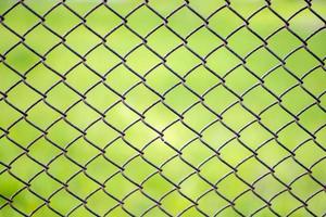 Mesh cage in the garden with green grass as background. Metal fence with wire mesh. Blurred view of the countryside through a steel iron mesh metal fence on green grass. Abstract background. photo