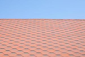 New roof with red shingles against the blue sky. High quality photo. Tiles on the roof of the house. Use to advertise roof fabrication and maintenance. Spotted texture. Affordable roofing. photo