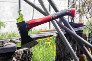 An ax with a red handle plunges into a stump. Sawmill operation concept. Woodworking. Stump and ax in sunny weather. Preparing firewood for the winter. Selective focus, blurred background. photo