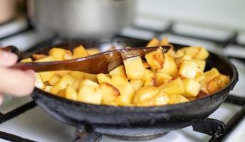 asar papas frescas en una sartén de hierro fundido con aceite de girasol. una vista de una estufa con una sartén llena de papas fritas doradas en una cocina real. comida cocinada en una sartén casera. foto