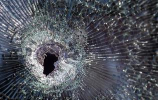 Bullet hole in glass with cracks, real bullet hole close-up. Authentic shot. The bullet made a cracked hole in the windshield of a car or a window glass shattered as a result of an accident. photo