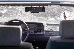 Broken windshield of a car from a bullet, from a shot from a firearm, view from the inside of the cabin. Damaged glass with traces of an oncoming stone on the road. Interior view of the car. photo