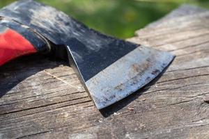 A sharp ax with an ergonomic rubberized handle on a wooden background. The ax is intended for rough, rough processing of wood. Has a forged heat treated carbon steel wedge. photo