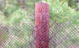 Mesh old ragged cage in the garden and a rusty pole with green grass as a background. Metal fence with wire mesh. Metal fence made of steel iron mesh. Abstract background. copy space. photo