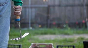 Caucasian woman gardener in the garden shows a rake. The concept of gardening and sustainable summer. Woman's hand with a garden tool. Chopper rake for gardening in female hands. Place for text. photo