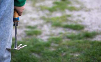 Caucasian woman gardener in the garden shows a rake. The concept of gardening and sustainable summer. Woman's hand with a garden tool. Chopper rake for gardening in female hands. Place for text. photo