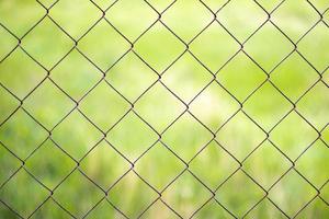 Mesh cage in the garden with green grass as background. Metal fence with wire mesh. Blurred view of the countryside through a steel iron mesh metal fence on green grass. Abstract background. photo