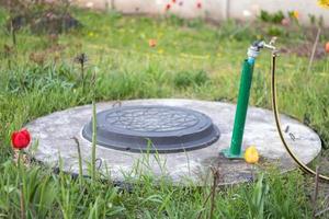 Plumbing, water pump from a well. An outside water faucet with a yellow garden hose attached to it. Irrigation water pumping system for agriculture. Hose in the garden for watering, sunny summer day. photo