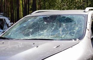 agujeros en el parabrisas del coche, fue disparado con un arma de fuego. agujeros de bala. rompa el parabrisas del coche, el coche roto y dañado. la bala hizo un agujero agrietado en el vidrio. foto