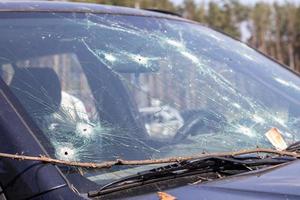 agujeros en el parabrisas del coche, fue disparado con un arma de fuego. agujeros de bala. rompa el parabrisas del coche, el coche roto y dañado. la bala hizo un agujero agrietado en el vidrio. foto