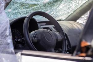 The steering wheel of a car after an accident. The driver's airbags did not deploy. View from the left side window. Broken windshield with steering wheel. Dusty black dashboard and steering wheel. photo