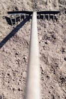 Close up photo of a garden rake on a bed. Old black metal rake on dry soil, in the garden. Spring cleaning. Selective focus. Yard area cleaning.