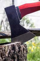 An ax with a red handle plunges into a stump. Sawmill operation concept. Woodworking. Stump and ax in sunny weather. Preparing firewood for the winter. Selective focus, blurred background. photo