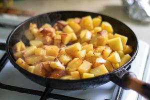 Roasting fresh potatoes in a cast iron skillet with sunflower oil. A view of a stovetop with a frying pan filled with golden fried potatoes in a real kitchen. Food cooked in a homemade frying pan. photo