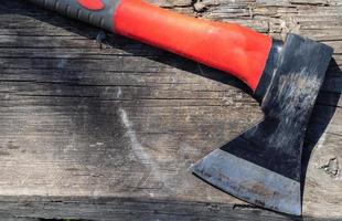 A sharp ax with an ergonomic rubberized handle on a wooden background. The ax is intended for rough, rough processing of wood. Has a forged heat treated carbon steel wedge. photo