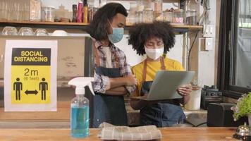 dos jóvenes socios cafe baristas y empresarios trabajan con máscara facial en una cafetería, esperando el pedido de los clientes en un nuevo servicio de estilo de vida normal, impacto comercial de la cuarentena pandémica covid-19. video