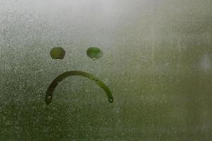 Face expession as boring and sad painted on window which fogged up after rain photo