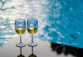 dos copas de vino blanco puestas en la mesa en la piscina para vacaciones y concepto de bebida de verano.