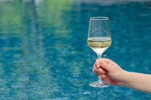 mano sosteniendo una copa de vino blanco con fondo de piscina. concepto de bebida de vacaciones y verano.