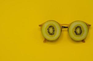 dos rodajas de kiwi dorado se ponen gafas de sol amarillas como cara. foto
