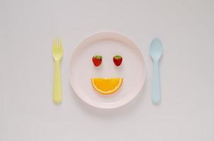 Strawberries  and cutting fresh orange fruit set as happy face on pink plate with fork and spoon on pastel background. Minimal creative healthy diet food concept. photo