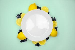 arándanos frescos y limón en la parte superior con plato blanco y fondo de color verde pastel para un concepto de comida saludable. foto