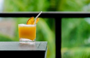 A glass of orange cocktail puts on table of the bar with green color background for Holiday and summer drink concept.