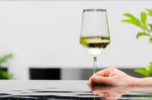 Hand holding a glass of white wine put on swimming pool. Holiday and summer drink concept. photo