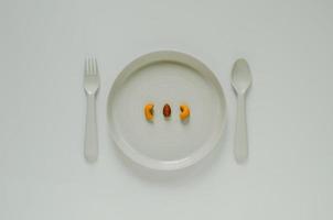 nuez de cajú y almendras en plato gris con tenedor y cuchara sobre fondo pastel. concepto de comida de dieta saludable creativa mínima. foto