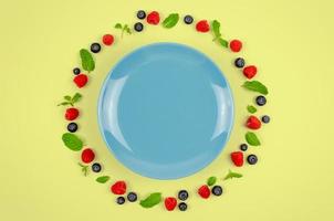 Fresh blueberries, raspberries and mint leaf on top view with blue plate and pastel yellow color background for healthy food concept. photo