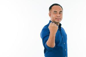 A self-confident middle age senior Asian man in a blue business casual shirt standing and showing the strong fist punch with copy space. Selective focus on hand. photo