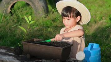 klein meisje met een hoed helpt haar moeder in de tuin, een kleine tuinman. schattig meisje planten bloemen in potten te koop. familie klein bedrijf video